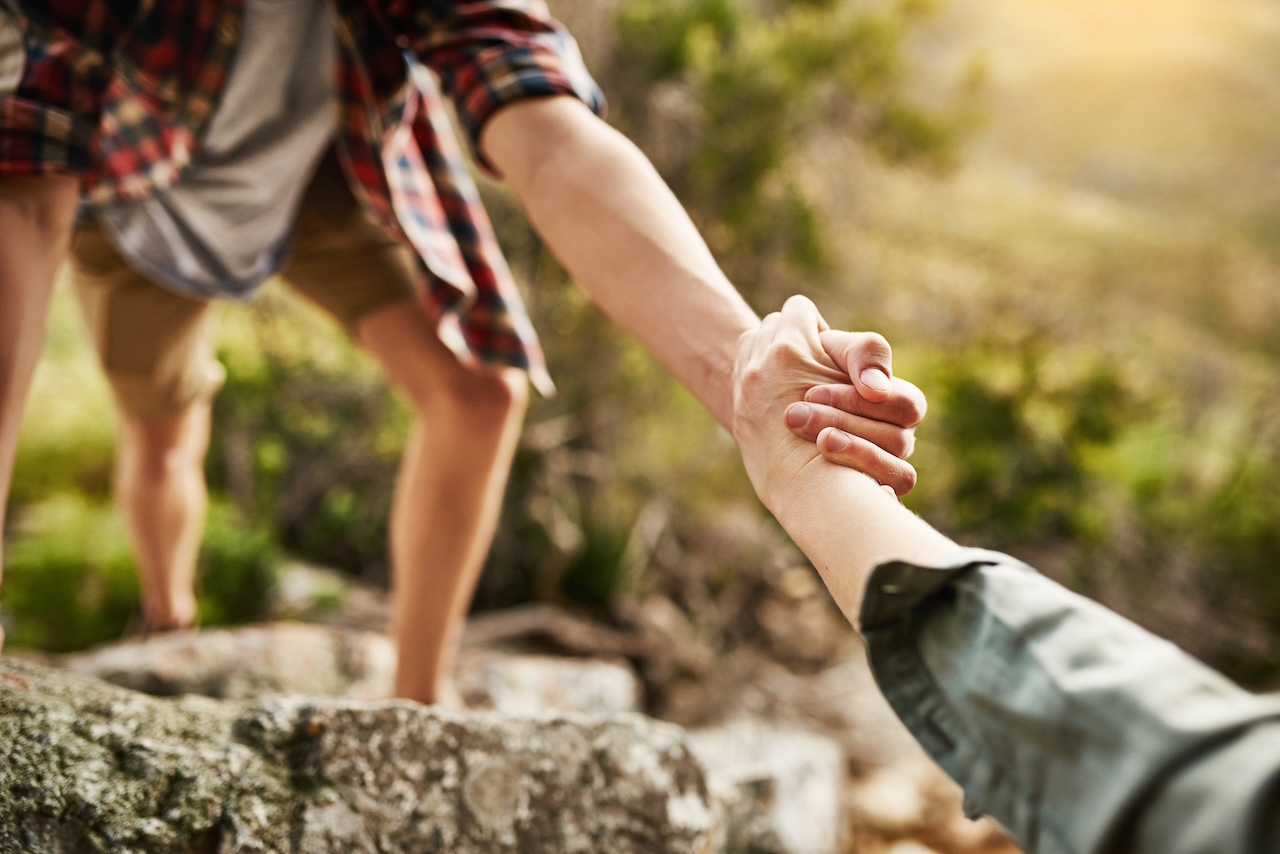 hombre sujetando de la mano a persona que está escalando