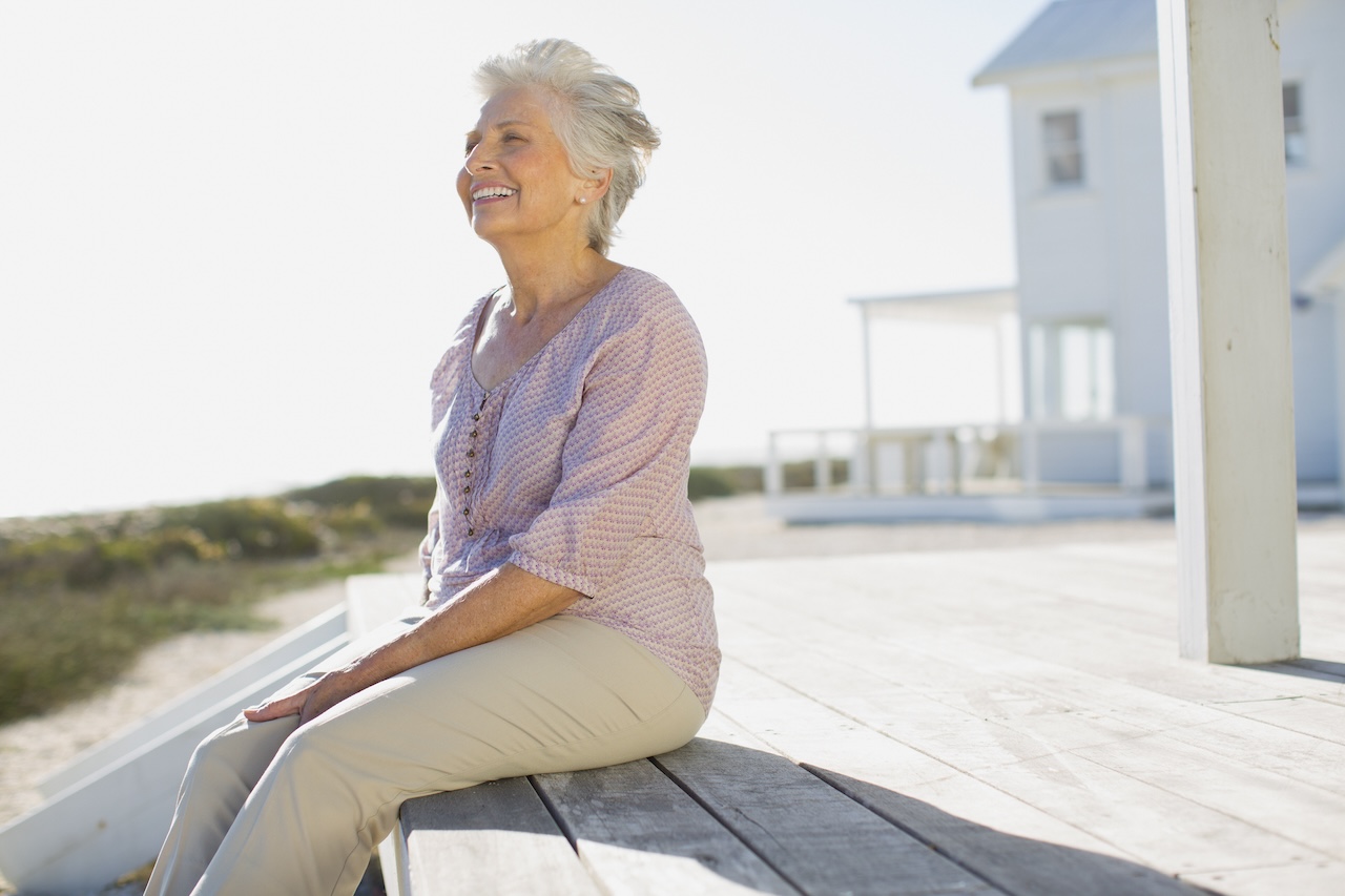 mujer anciana sentada en porche de casa de playa sonriendo