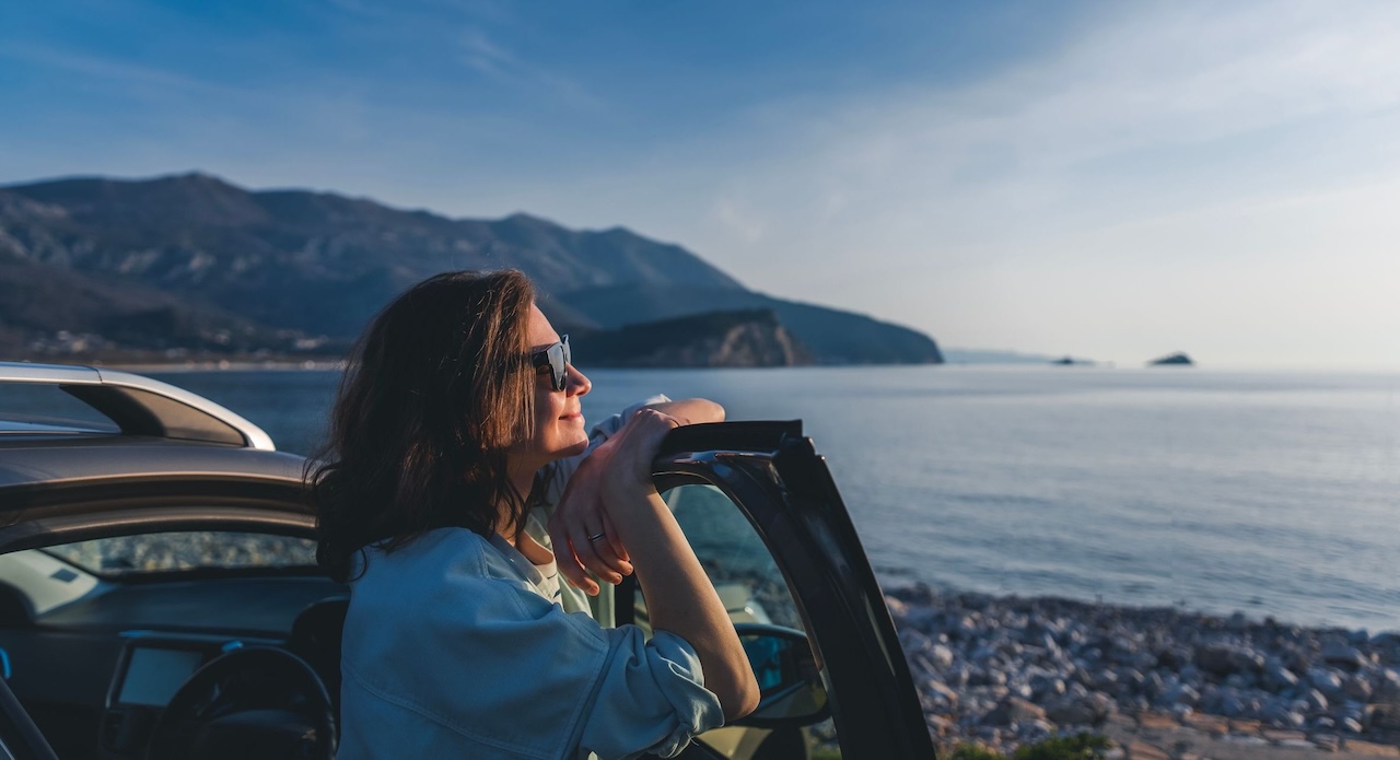 mujer en la playa apoyada sobre la ventana de un coche