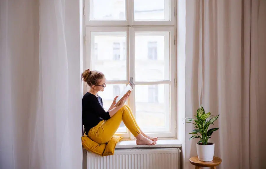 mujer sentada en repisa de ventana leyendo