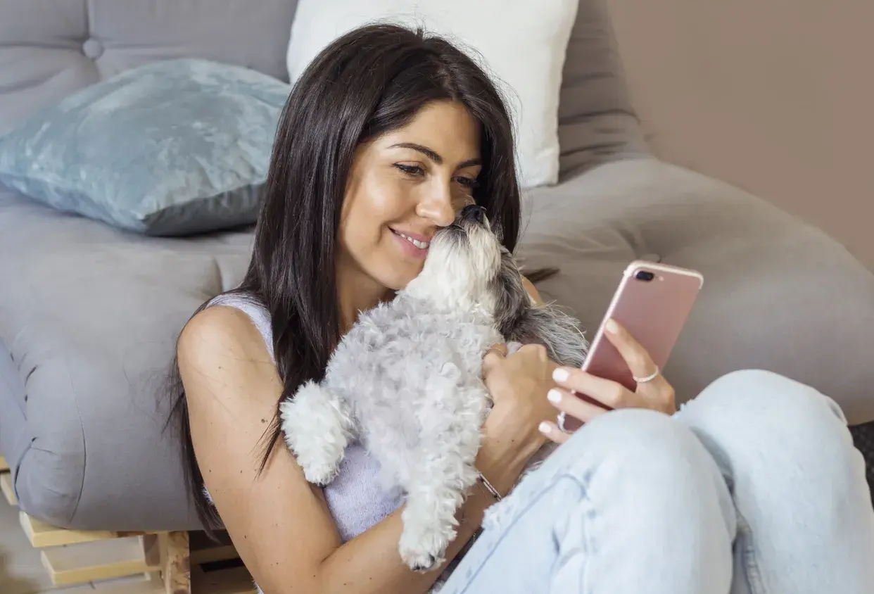 mujer abrazando a su mascota mientras utiliza un móvil